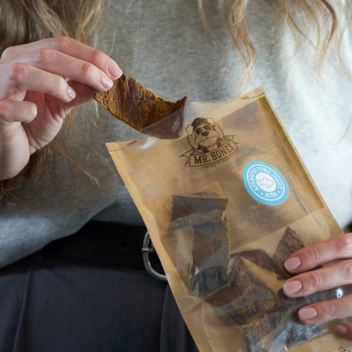 Hand håller en bit tonfiskjerky framför påsen