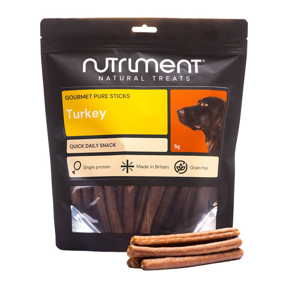 Nutriment Gourmet Pure Sticks Kalkon 1kg, stor svart påse med gul etikett och godispinnar framför, mot vit bakgrund